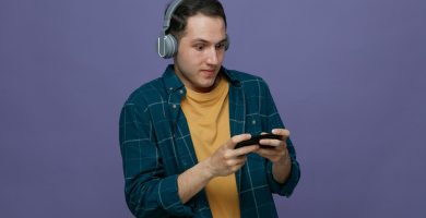 impressed young male student wearing headphones playing interactive games on mobile phone