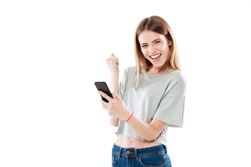 Woman holding mobile phone and celebrating a win in advergaming isolated over white background