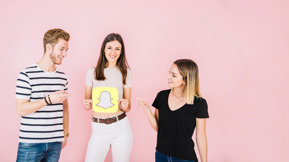 Man and woman pointing at their happy friend holding snapchat icon
